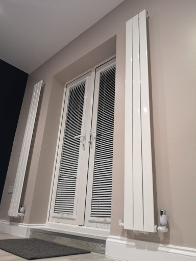 Two tall, white radiators beside a set of double doors with blinds.