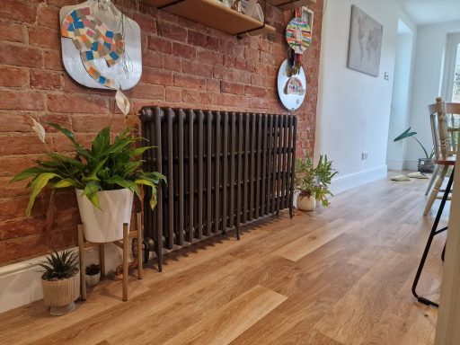 A cosy interior featuring a brick wall, wooden flooring, radiator, and decorative plants.