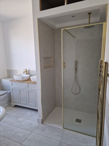 Modern bathroom featuring a glass shower, sink, and light tiles.
