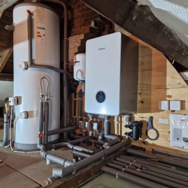 Boiler and hot water tank with connected pipes in a loft.