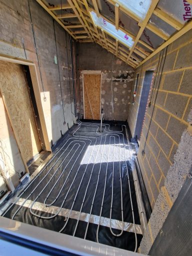 Interior of a building under construction with visible heating pipes and insulated walls.